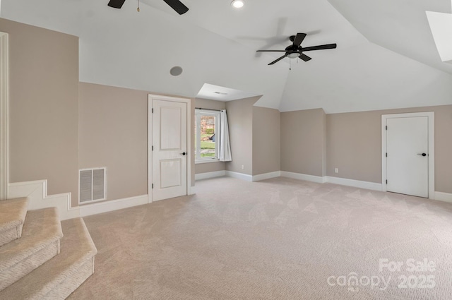 additional living space with light colored carpet, lofted ceiling with skylight, baseboards, visible vents, and a ceiling fan