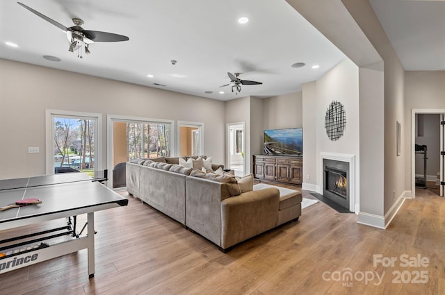 living area featuring a fireplace with flush hearth, light wood finished floors, baseboards, recessed lighting, and a ceiling fan