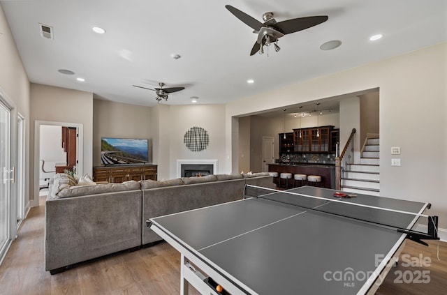 playroom with a warm lit fireplace, light wood-type flooring, recessed lighting, and a ceiling fan