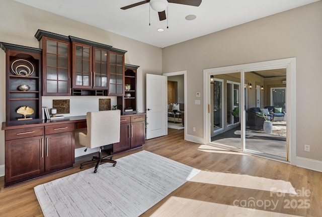 home office with baseboards, built in study area, light wood-style flooring, and a ceiling fan