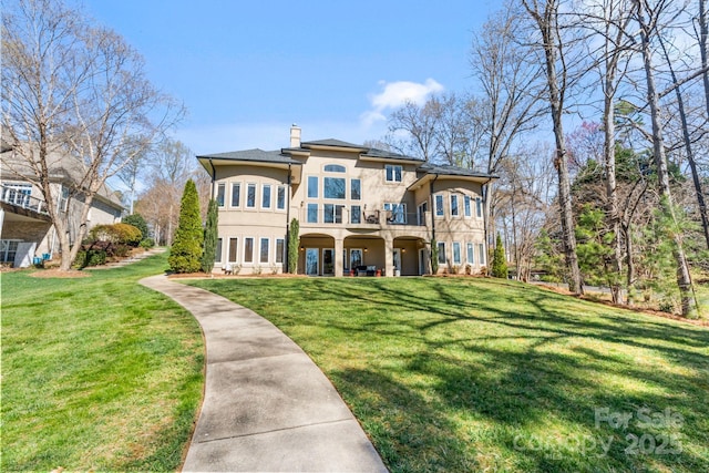 back of property featuring a balcony, stucco siding, a yard, and a chimney