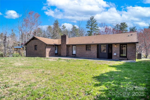 back of house featuring a chimney, central AC, brick siding, and a yard
