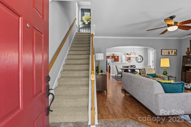 living area featuring arched walkways, wood finished floors, stairs, ceiling fan, and crown molding