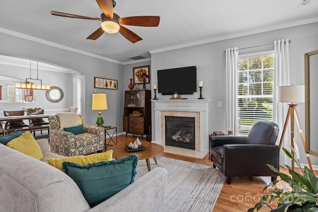living area with crown molding, wood finished floors, ceiling fan with notable chandelier, a fireplace, and visible vents