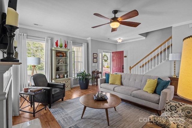 living area featuring wood finished floors, visible vents, ornamental molding, stairs, and ceiling fan