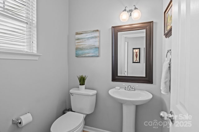 half bath featuring baseboards, a sink, and toilet