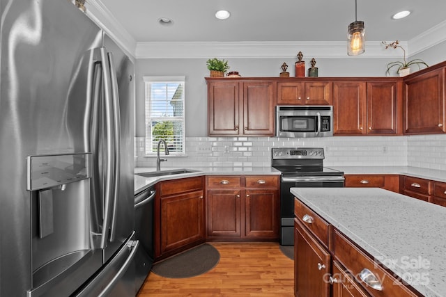 kitchen with a sink, decorative backsplash, light wood-style floors, appliances with stainless steel finishes, and ornamental molding
