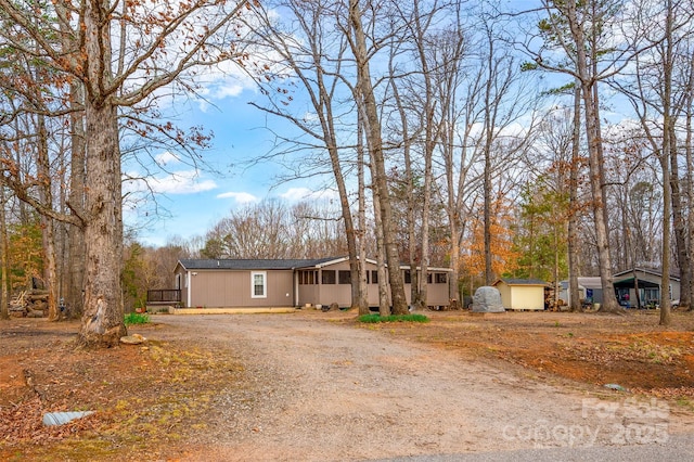 view of front facade featuring an outdoor structure, a sunroom, driveway, and a shed