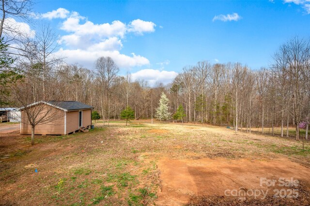 view of yard with an outbuilding, a view of trees, and a storage shed