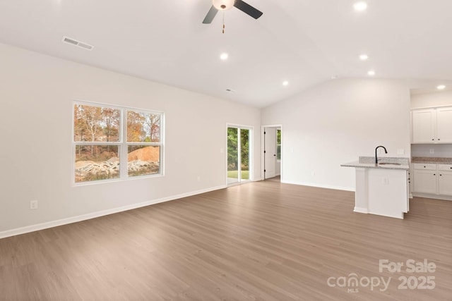 unfurnished living room with a sink, visible vents, vaulted ceiling, and light wood finished floors