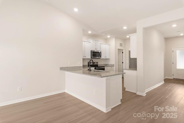 kitchen with light wood finished floors, a peninsula, a sink, stainless steel appliances, and white cabinetry