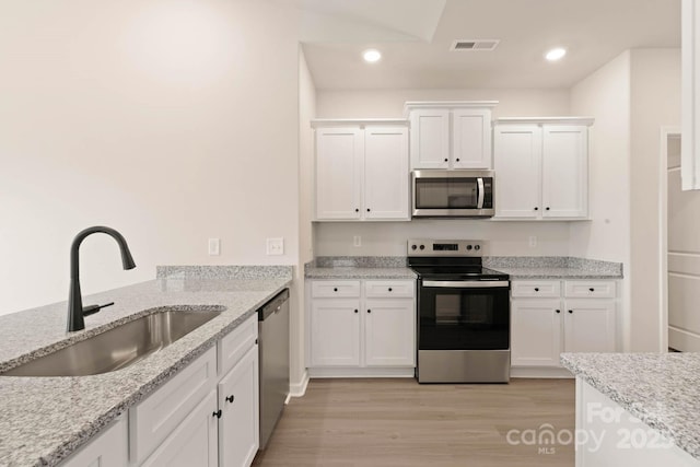 kitchen featuring visible vents, light wood-style flooring, a sink, white cabinetry, and appliances with stainless steel finishes