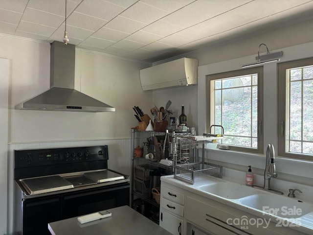 kitchen with black / electric stove, light countertops, wall chimney range hood, white cabinets, and a sink