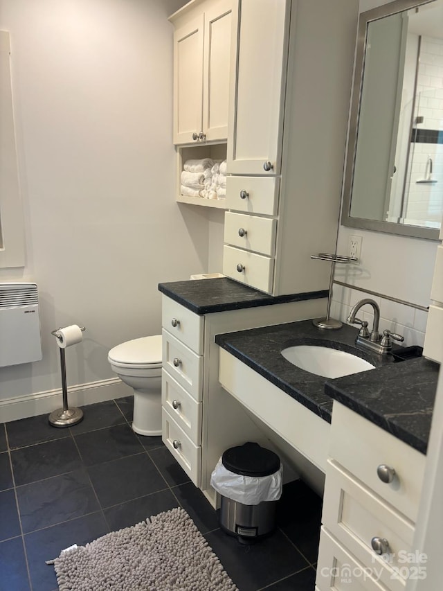bathroom with heating unit, tile patterned flooring, toilet, vanity, and baseboards