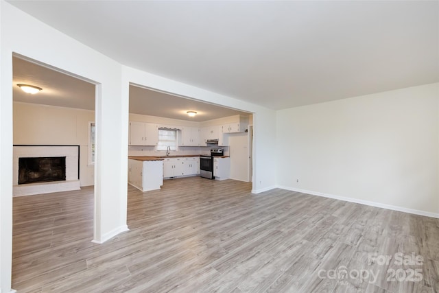 unfurnished living room featuring a brick fireplace, baseboards, light wood-style floors, and a sink