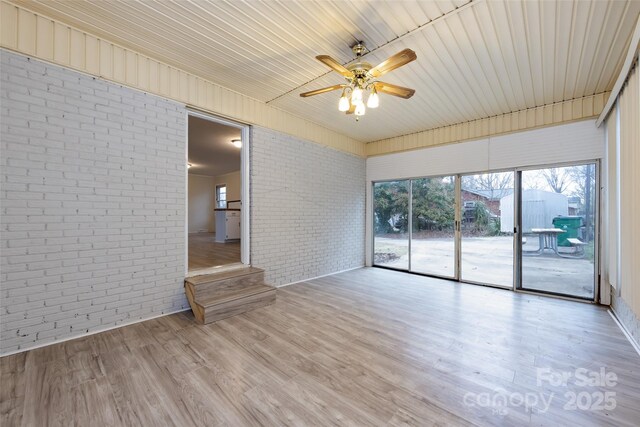 spare room featuring brick wall, a ceiling fan, and wood finished floors
