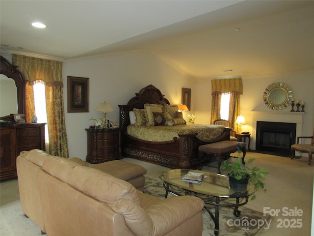 bedroom featuring a fireplace with flush hearth, lofted ceiling, crown molding, and light colored carpet