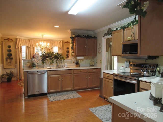 kitchen featuring light countertops, crown molding, appliances with stainless steel finishes, a sink, and an inviting chandelier