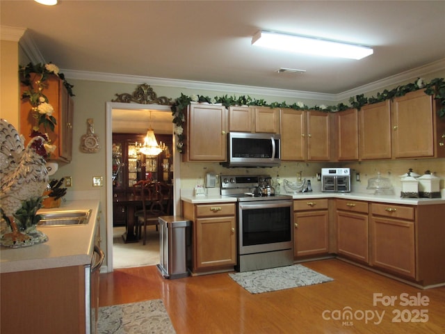 kitchen featuring crown molding, light countertops, light wood-style flooring, stainless steel appliances, and an inviting chandelier