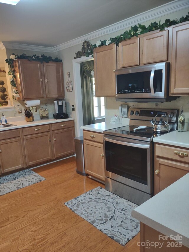 kitchen featuring light countertops, crown molding, stainless steel appliances, a sink, and light wood finished floors