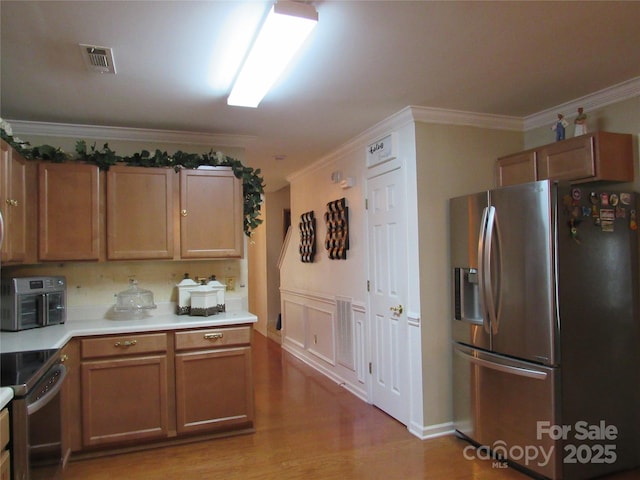 kitchen with light countertops, crown molding, stainless steel appliances, light wood-style floors, and visible vents