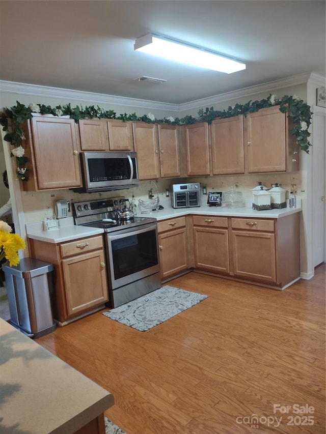 kitchen featuring light wood finished floors, light countertops, ornamental molding, and stainless steel appliances