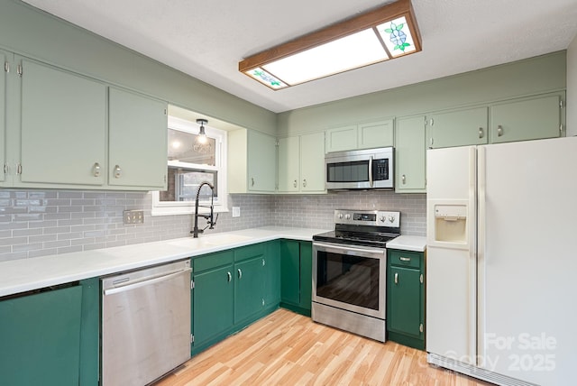 kitchen featuring light countertops, light wood-type flooring, backsplash, a sink, and appliances with stainless steel finishes