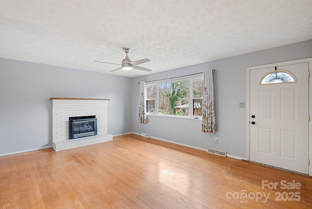 unfurnished living room featuring a brick fireplace, visible vents, a ceiling fan, and light wood finished floors