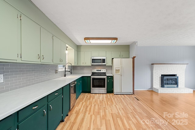 kitchen featuring green cabinets, light wood-style flooring, a sink, and appliances with stainless steel finishes