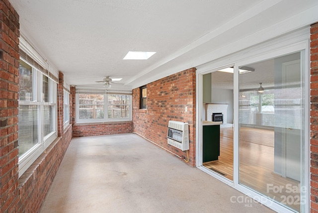 unfurnished sunroom with heating unit, plenty of natural light, a skylight, and brick wall