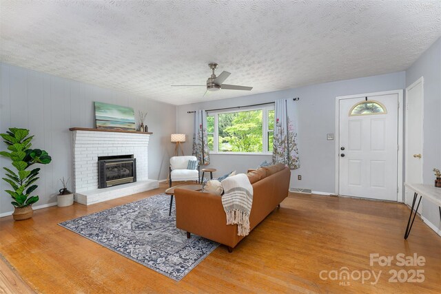 31 Vista Dr, Candler, NC 28715 - living room featuring wood finished floors, a ceiling fan, a fireplace, a textured ceiling, and baseboards