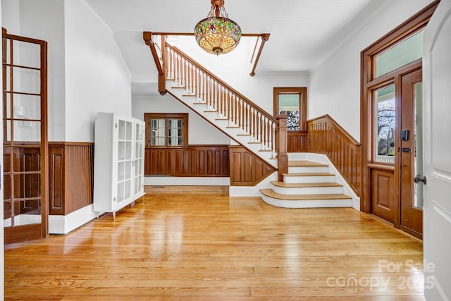 entryway featuring crown molding, a chandelier, a wainscoted wall, stairway, and light wood-style flooring