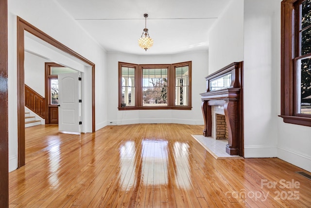 unfurnished living room with stairway, visible vents, baseboards, a fireplace, and light wood-style floors