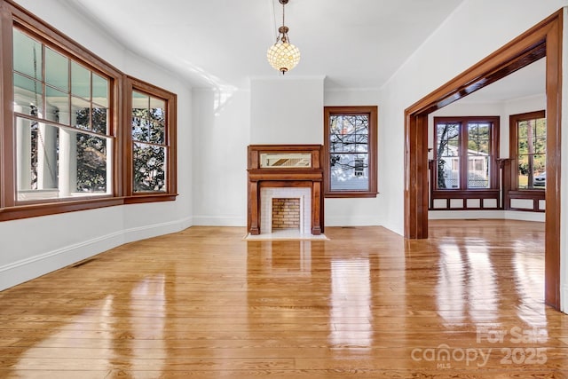 unfurnished living room with baseboards, a fireplace with flush hearth, light wood-style flooring, and ornamental molding