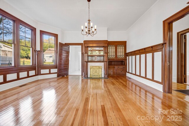 unfurnished living room featuring ornamental molding, light wood-style floors, visible vents, and a chandelier