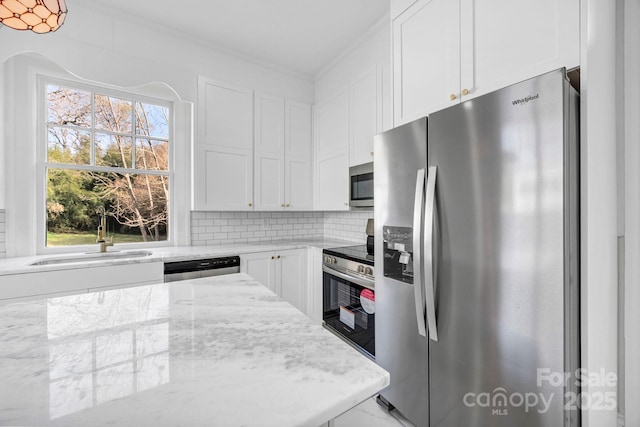 kitchen featuring light stone counters, decorative backsplash, white cabinets, stainless steel appliances, and a sink