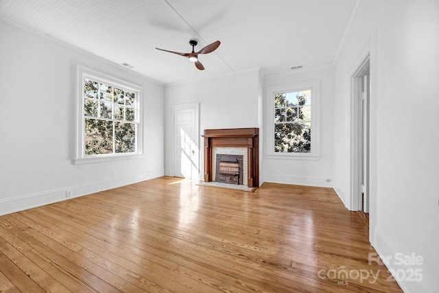 unfurnished living room featuring a wealth of natural light, wood-type flooring, a fireplace, and a ceiling fan