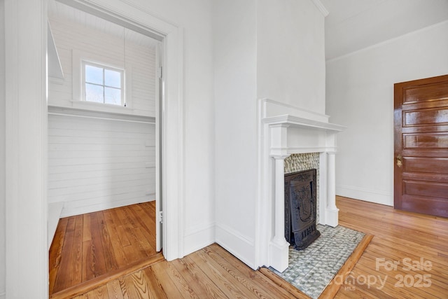unfurnished living room featuring a fireplace with flush hearth, ornamental molding, baseboards, and wood finished floors