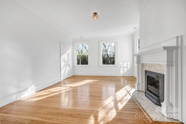 unfurnished living room featuring a fireplace with flush hearth, baseboards, light wood-style floors, and ornamental molding