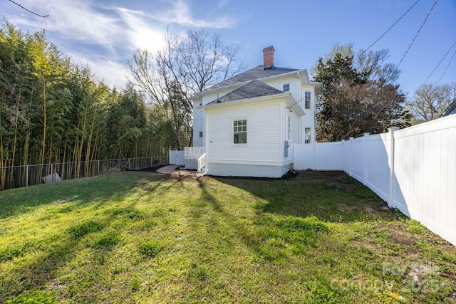 rear view of house with a fenced backyard, a chimney, and a yard