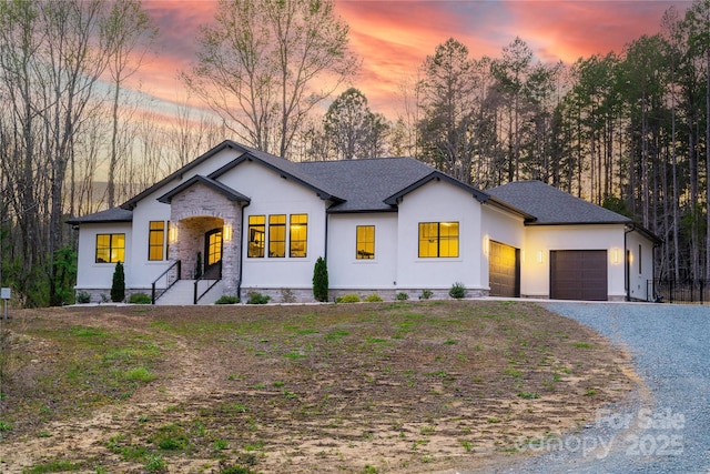 modern inspired farmhouse featuring gravel driveway, stucco siding, a garage, and roof with shingles
