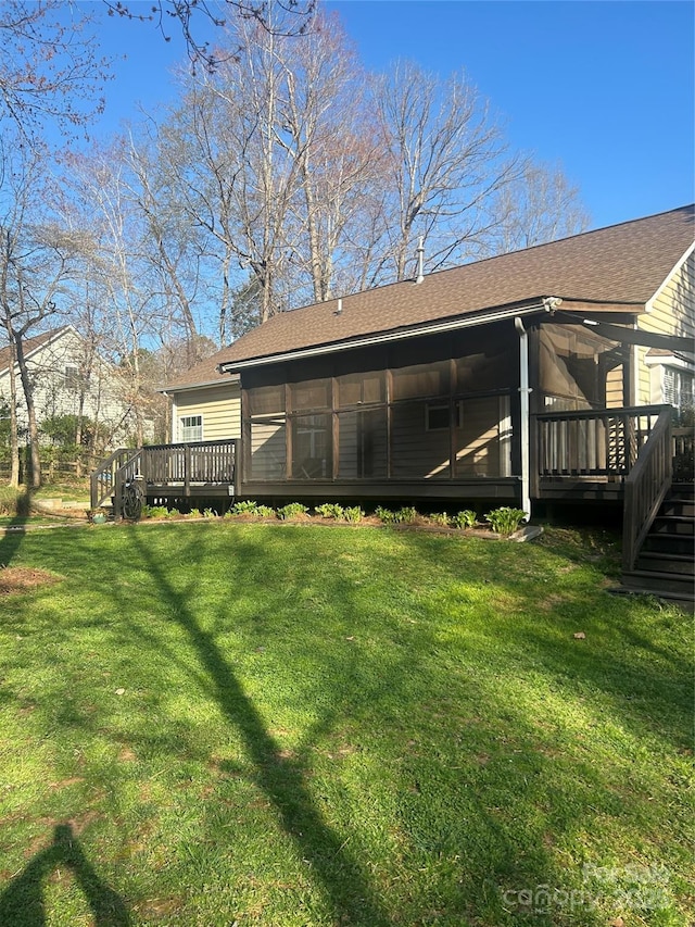 rear view of house featuring a deck, a sunroom, a yard, and roof with shingles