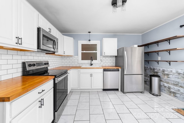 kitchen featuring butcher block counters, ornamental molding, stainless steel appliances, white cabinetry, and a sink
