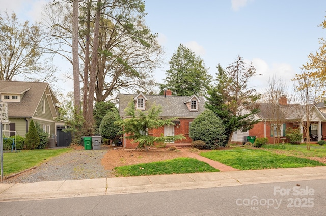 view of front facade with brick siding, gravel driveway, a front lawn, and a shingled roof
