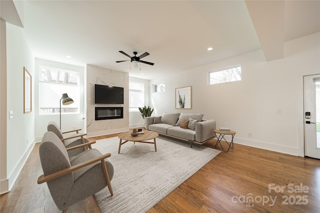 living room with a premium fireplace, recessed lighting, baseboards, ceiling fan, and wood finished floors