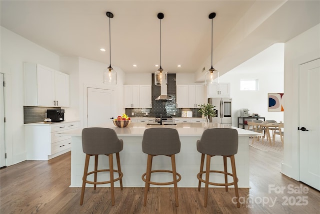 kitchen with a sink, stainless steel fridge with ice dispenser, wall chimney exhaust hood, wood finished floors, and a large island