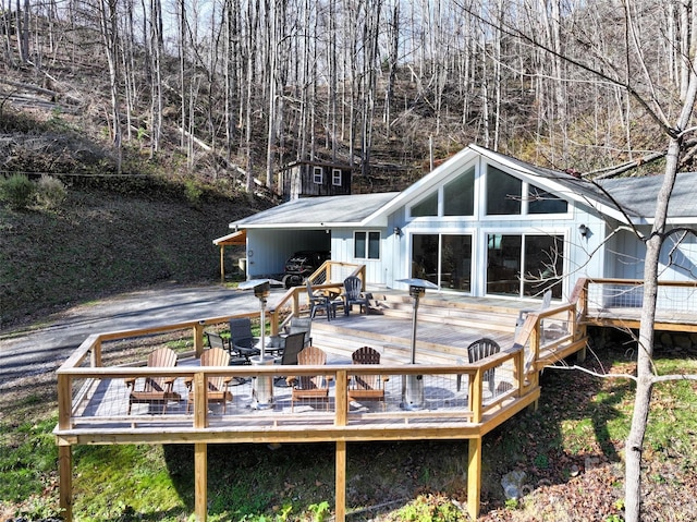 rear view of property featuring driveway, a carport, and a wooden deck