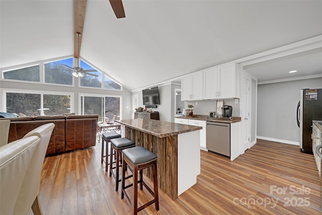 kitchen featuring a ceiling fan, lofted ceiling with beams, a kitchen bar, appliances with stainless steel finishes, and open floor plan