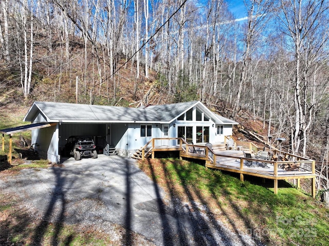 view of front facade featuring a wooden deck, aphalt driveway, a shingled roof, a carport, and a wooded view