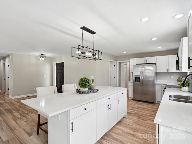 kitchen with a sink, a kitchen island, light wood finished floors, a kitchen bar, and stainless steel refrigerator with ice dispenser
